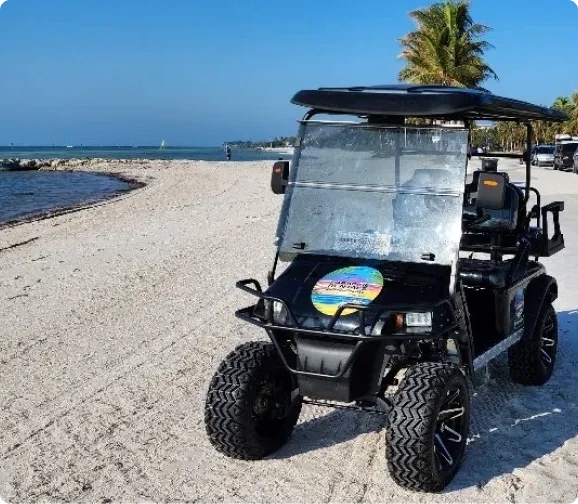Paradise Rentals KW black electric golf cart with rugged off-road tires parked on a wide, sunny Key West beach
